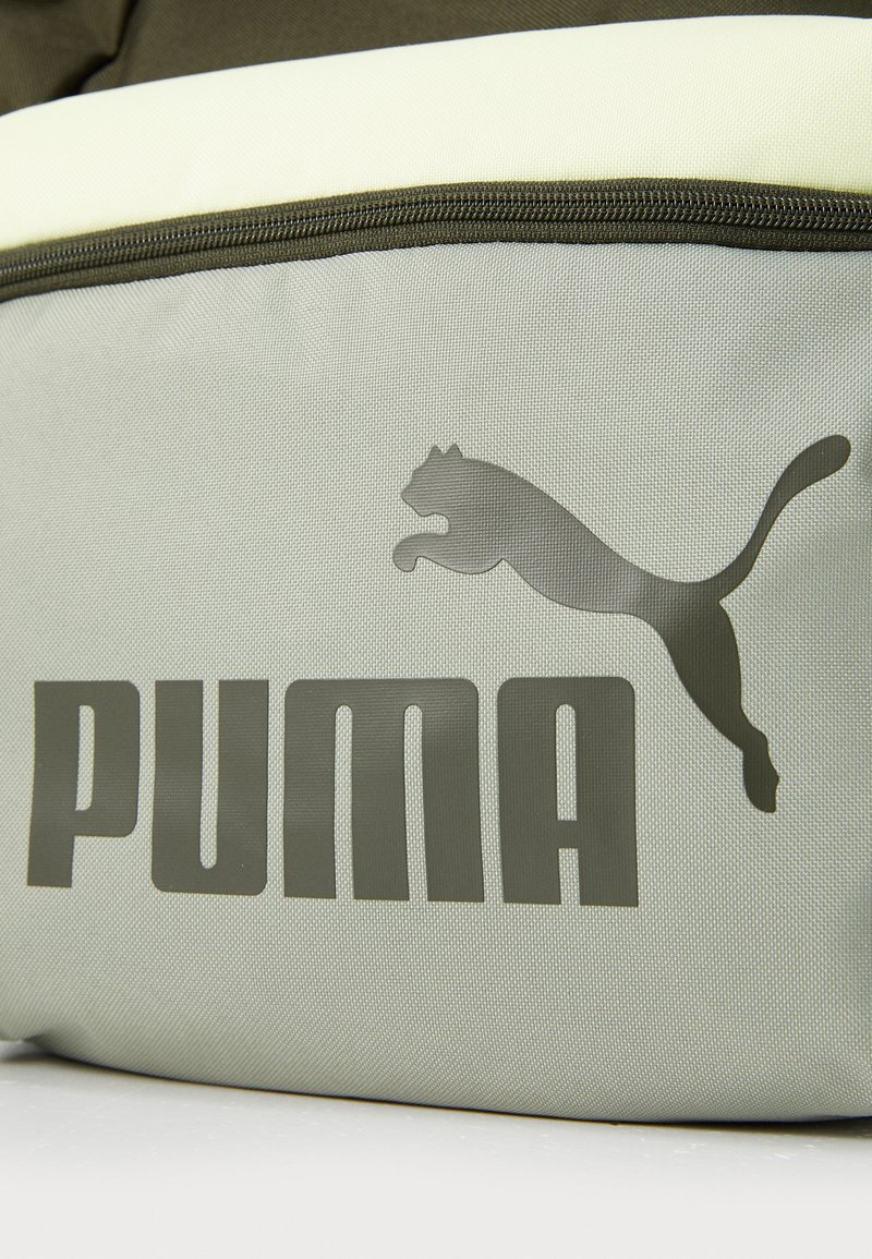 Pochette en tissu vert avec un dessus lisse jaune clair. Comprend un grand logo "PUMA" gris foncé et un graphique de puma en saut. Fermeture zippée.