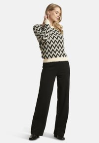 Black and cream zigzag patterned knit sweater, featuring a soft texture, wide cuffs, and a fitted waist, paired with black wide-leg trousers.
