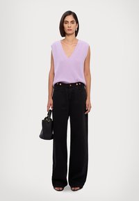 Top din tricot lavandă fără mâneci cu decolteu în V, asortat cu pantaloni evazați negri cu talie înaltă. O geantă neagră și sandale cu vârf deschis completează ținuta.