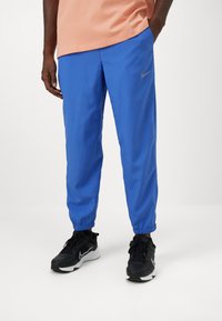 Blue, lightweight athletic pants with an elastic waistband and ankle cuffs, featuring a subtle gold Nike logo on the left thigh.
