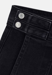 Primo piano di una vita in denim nero con doppi bottoni a pressione argentati e passanti per cintura, che mostrano dettagli di cucitura e texture del tessuto.