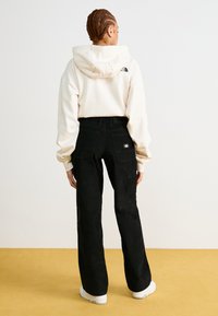 Μαύρο παντελόνι καμπάνα με πλαϊνέ�ς τσέπες, συνδυασμένο με μια κρεμ φούτερ με κουκούλα που έχει ένα μαύρο λογότυπο στην πλάτη. Φορούνται λευκά sneakers.