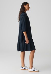 Abito a balze di colore blu navy con maniche puff a tre quarti, vestibilità comoda, abbinato a sneakers bianche con strisce navy e suola in gomma.