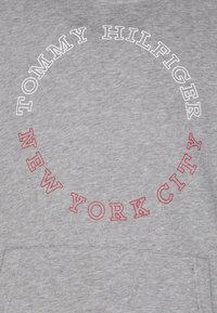 Grauer Sweatshirt mit einem kreisförmigen gestickten Logo, das "TOMMY HILFIGER" in Weiß und "NEW YORK CITY" in Rot zeigt, zentriert auf der Brust.