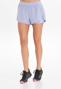 Lichtpaarse sportshorts met een elastische band, zijsplitten en een ademende stof. Draagt met zwarte sneakers met roze zolen.