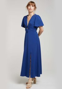 Robe maxi bleue avec des manches courtes évasées, un décolleté en V profond avec un détail à nouer, et une fente à l'avant. Texture lisse, tissu léger.