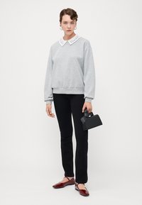 Grauer Sweatshirt mit einem weißen, gestickten Kragen, schwarzen, enganliegenden Jeans, roten Slippern und einer kleinen schwarzen Handtasche.