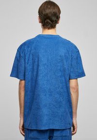Blå oversized t-skjorte med et mykt, teksturert stoff. Har rund hals og korte ermer. Enkel, udekorerte design.
