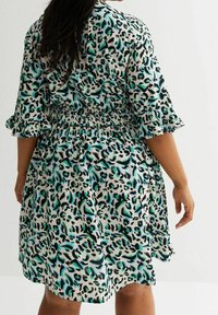 Short-sleeve dress featuring a black, teal, and white leopard print, with a fitted waist and flared skirt, made from a lightweight fabric.