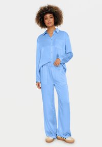 Light blue loungewear set featuring a button-up shirt with a chest pocket and elastic waistband pants. Smooth texture with relaxed fit.