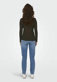 Long-sleeve, ribbed, dark green top paired with light blue jeans and white sneakers. Curly hair falls to the shoulders.