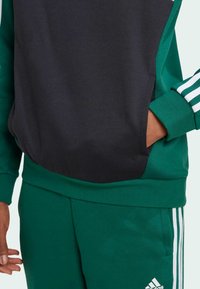 Sudadera verde y negra con un bolsillo, puños acanalados y tres rayas blancas en las mangas, hecha de un tejido suave.