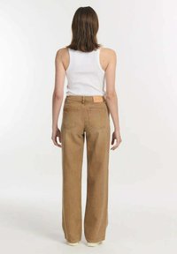 Lichtbruine wijde jeans met een hoge taille, voorzien van achterzakken en een merklabel op de tailleband. Katoenen stof, minimale details.