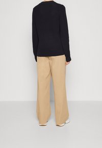 Pull en maille bleu marine à manches longues, col rond et taille ajustée, associé à un pantalon beige à jambes larges et des baskets blanches.