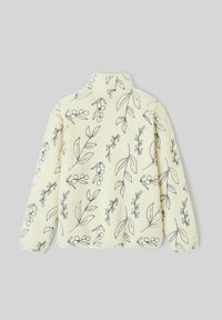 Veste polaire crème avec broderie florale noire, col haut et manches longues. Texture douce, ornée de motifs de feuilles et de baies.