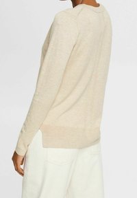 Jasnobeżowy sweter z długim rękawem o teksturowanym wykończeniu, z prążkowanymi mankietami i dołem, oraz nieco dłuższym tyłem. Prosty i minimalistyczny design.