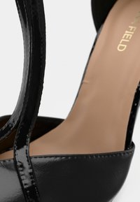 Κλείσιμο εικόνας του μαύρου λουστρίνι ψηλού τακουνιού σανδάλι με μπεζ πέλμα και λεπτά λουράκια.