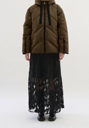 Ruskea vuorattu takki hupulla, jossa on mustat kiristysnyörit ja vetoketjut; pitkä musta pitsihame on sen päällä. Mustat nilkkurit täydentävät asua.