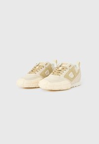 Μπεζ αθλητικά παπούτσια με υφασμάτινο επάνω μέρος με υφή, τονικά σουέντ διακριτικά στοιχεία και χοντρή λαστιχένια σόλα. Στρογγυλεμένο σχήμα με κορδόνια και θηλιά για κράτημα.