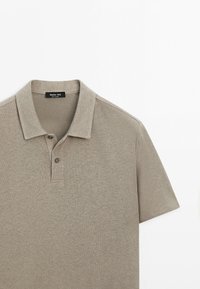 Polo beige à manches courtes avec col et deux boutons, montrant la moitié supérieure et l’étiquette de la marque à l’intérieur du col.