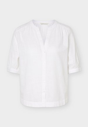 Witte blouse met korte mouwen, mandarijnkraag, knoopsluiting aan de voorkant en lichte plooitjes op de schouders en manchetten.
