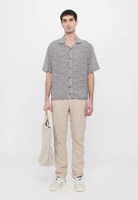 Košeľa s krátkym rukávom s geometrickým vzorom v šedej a bielej farbe, doplnená béžovými ľanovými nohavicami a bielymi teniskami. Bavlnená taška.