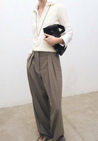 Jasny, długi rękaw z dekoltem w szpic, zestawiony z wysokim stanem, plisowanymi brązowymi spodniami. Mała czarna torebka i duży naszyjnik.