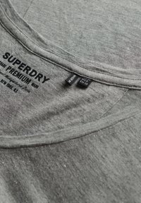 Graues Baumwoll-T-Shirt mit Rundhalsausschnitt und dem Schriftzug "SUPERDRY" in Schwarz. Mit Größenetiketten: US 6, EU 38, und Pflegehinweisen.