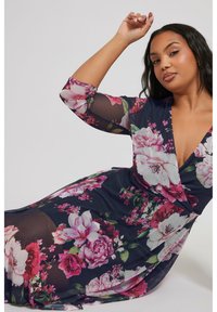 Kukkakuvioinen mekko, jossa on pitkät läpinäkyvät hihat. Koristeena eloisia vaaleanpunaisia ja valkoisia kukkia tummansinisellä taustalla. V-pääntie ja laskostettu siluetti.