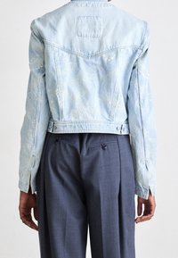 Ljusblå denimjacka med detaljerad vit blommönstring på baksidan, i kort modell, med knappstängning och långa ärmar.