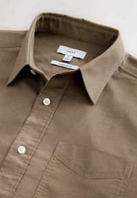 Camisa de botones marrón de algodón, con un corte clásico, cuello puntiagudo, bolsillo frontal y cierre de botones blancos. Incluye etiquetas.