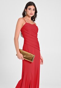 Rotes Abendkleid mit Herz-Ausschnitt, gerafftem Oberteil und fließendem Rock. Kombiniert mit einer goldenen metallischen Clutch.
