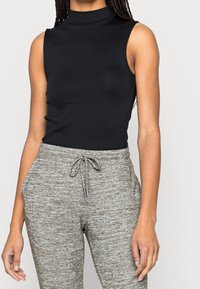 Svart ärmlös polotröja i kombination med grå, texturerade sweatpants med dragsko i midjan och elastiska manschetter.