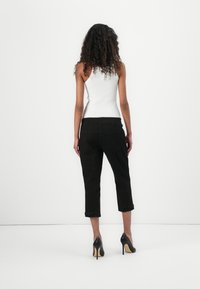 Jeans negros cortos con dobladillo plegado, combinados con una camiseta sin mangas blanca ajustada y zapatos de tacón altos negros. Modelo visto desde la parte de atrás.