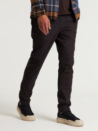 Pantaloni neri realizzati in tessuto elastico e leggero; design aderente con texture liscia e tasche laterali. Indossati con sneaker nere.