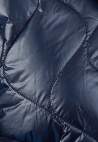 Tessuto trapuntato blu navy con finitura lucida, che mostra cuciture a forma di rombo e una superficie liscia con imbottitura morbida.