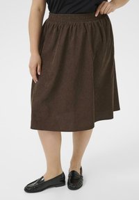 Brown, knee-length skirt made from textured fabric with an elastic waistband. Paired with black loafers.