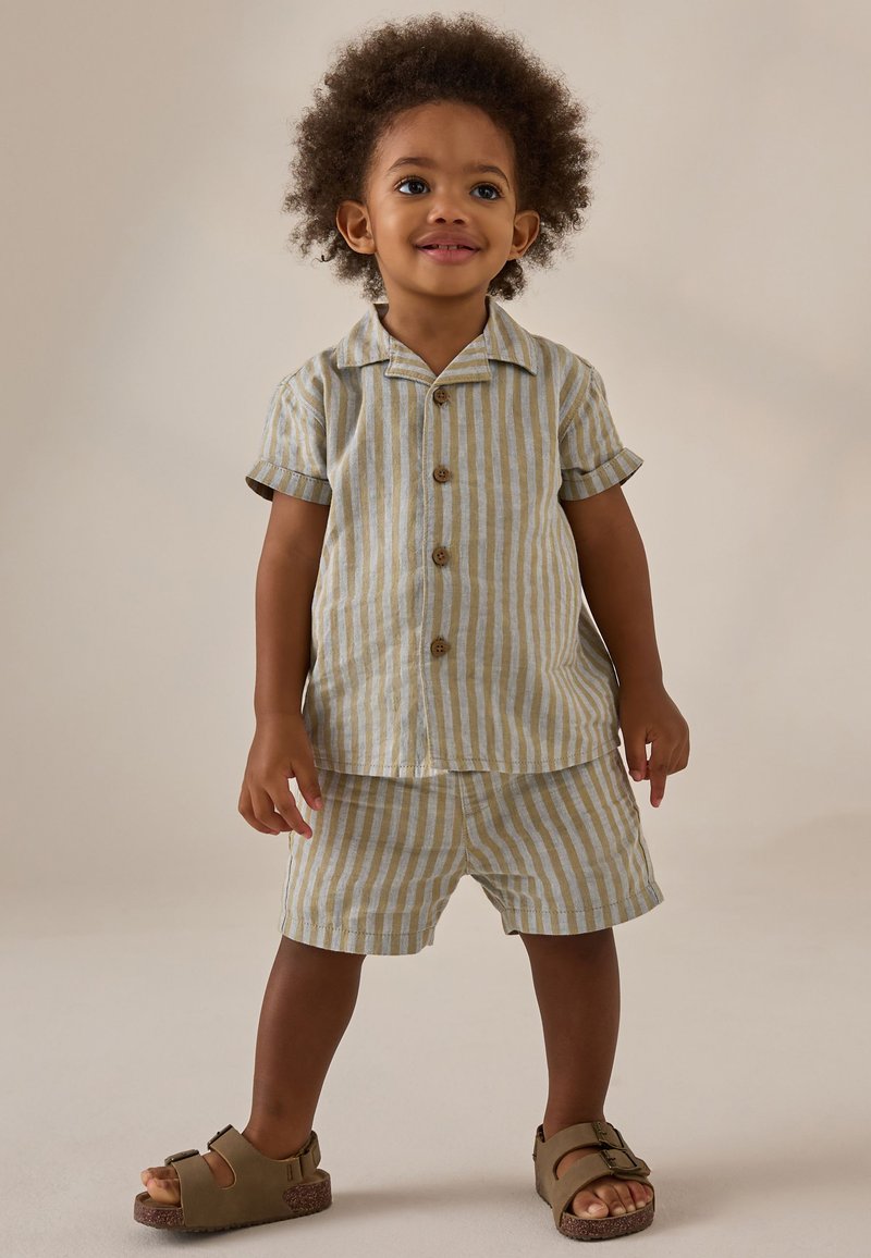 Conjunto de camisa de manga corta y pantalones cortos a rayas en beige claro y azul. Cuenta con botones de madera y un corte relajado. Combinado con sandalias marrones.