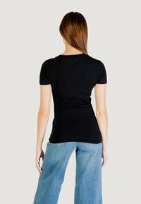 T-shirt nero a maniche corte con design aderente, texture liscia e scollatura rotonda, indossato con jeans a gamba larga blu.