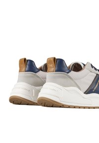 Sneakers da uomo in beige, navy e tan, realizzati in pelle e suede, con una spessa suola bianca e un dettaglio di branding sul tallone.