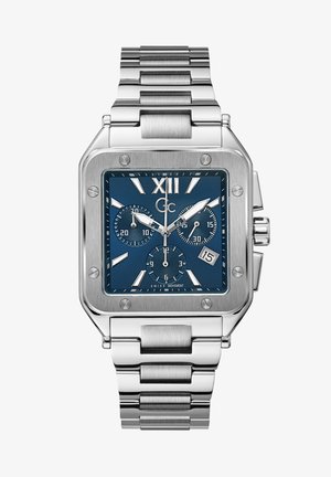 Kvadrāta formas nerūsējošā tērauda pulkstenis ar zilu ciparnīcu, sudraba akcentiem, hronogrāfu apakšizliekumiem un datuma displeju; aprīkots ar savienotu metāla siksnu.