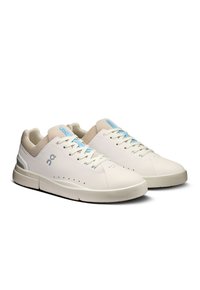Białe sportowe sneakersy z gładką skórzaną cholewką, siateczkowym kołnierzem, siateczkowym językiem i jasnoniebieskimi akcentami na sznurówkach oraz logo. Gruba gumowa podeszwa.