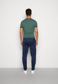 Camiseta verde de manga corta con ribete azul oscuro, combinada con un pantalón jogging azul oscuro con un patrón de diamantes y zapatillas blancas.