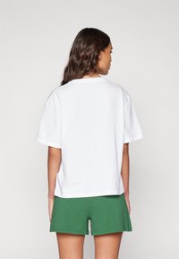T-shirt blanc à coupe décontractée, à manches courtes et col côtelé, associé à un short vert. Design simple, uni, sans motifs.