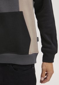 Genser med fargeblokker i svart, beige og mørkegrå. Har en lomme foran og ribbestrikkede mansjetter og nederkant.