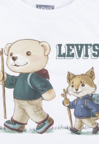 Bela majica s crtanim likom medveda in lisice, oba z nahrbtniki in pohodniškimi palicami; nad njimi je v zelenem napisan "LEVI'S".