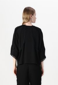 Black top featuring a loose fit, short sleeves, and fringed accents along the seams. Material appears soft with a matte finish.