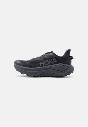 Schwarz-grauer HOKA Trailrunning-Schuh mit dicker Sohle, Obermaterial aus Mesh und Lasche an der Ferse, seitlich auf weißem Hintergrund dargestellt.