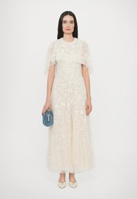 Maximekko vaaleassa beigevärisessä kukka-embroidereissa, läpikuultavissa leijailevissa hihoissa ja lentävässä siluetissa. Yhdistettynä pieneen siniseen käsilaukkuun ja vaaleisiin korkokenkiin.