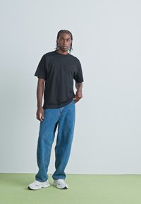 T-shirt noir à manches courtes associé à un jean en denim bleu ample, accompagné de baskets blanches. Design simple, coupe décontractée, détails minimalistes.